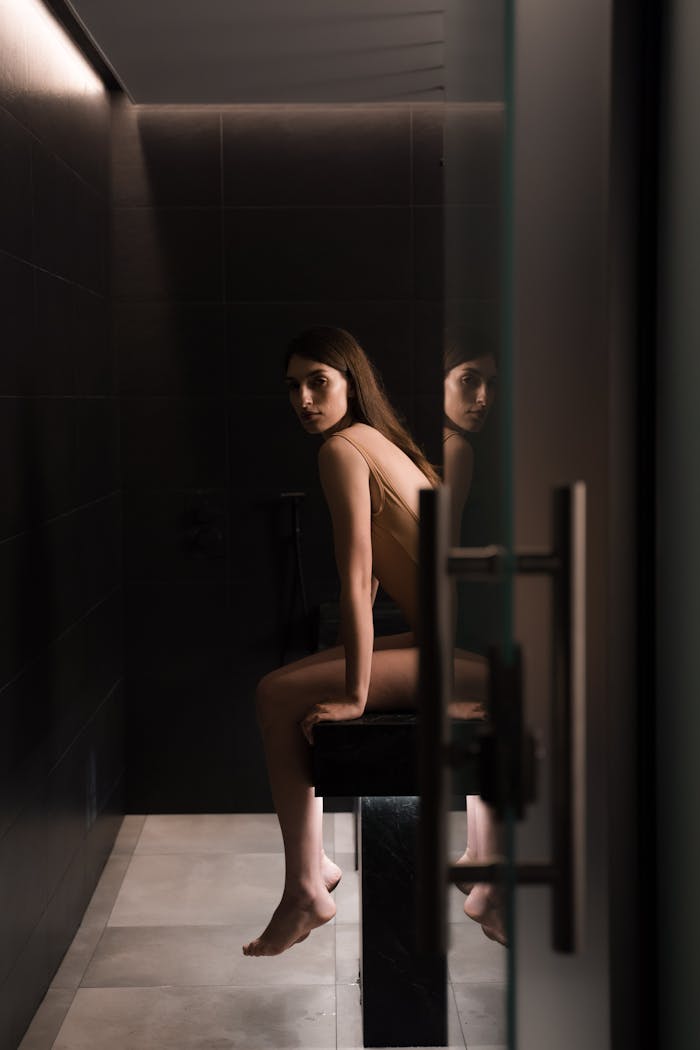 hero-img-02 Woman in swimsuit seated in a dimly lit sauna room, enjoying relaxation and tranquility.